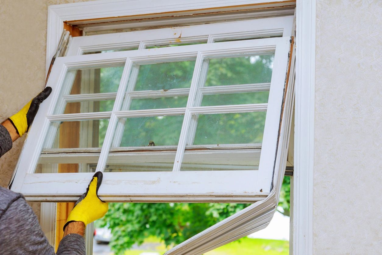 A person with yellow gloves pointing to an open window.